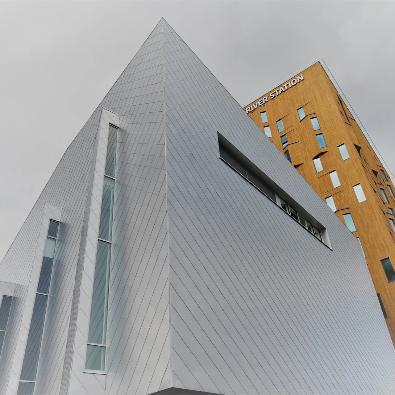 En moderne bygning med geometrisk metall- og trefasade står mot en skyet himmel. Teksten på treseksjonen lyder "RIVER STATION".
