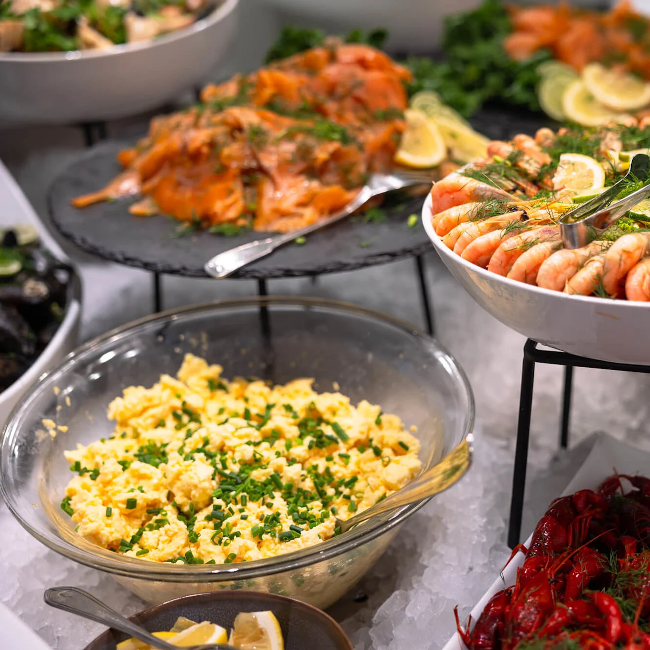Reker arrangert i en bolle, pyntet med sitronskiver og dill, står på en buffet sammen med eggerøre og kreps, omgitt av is.
