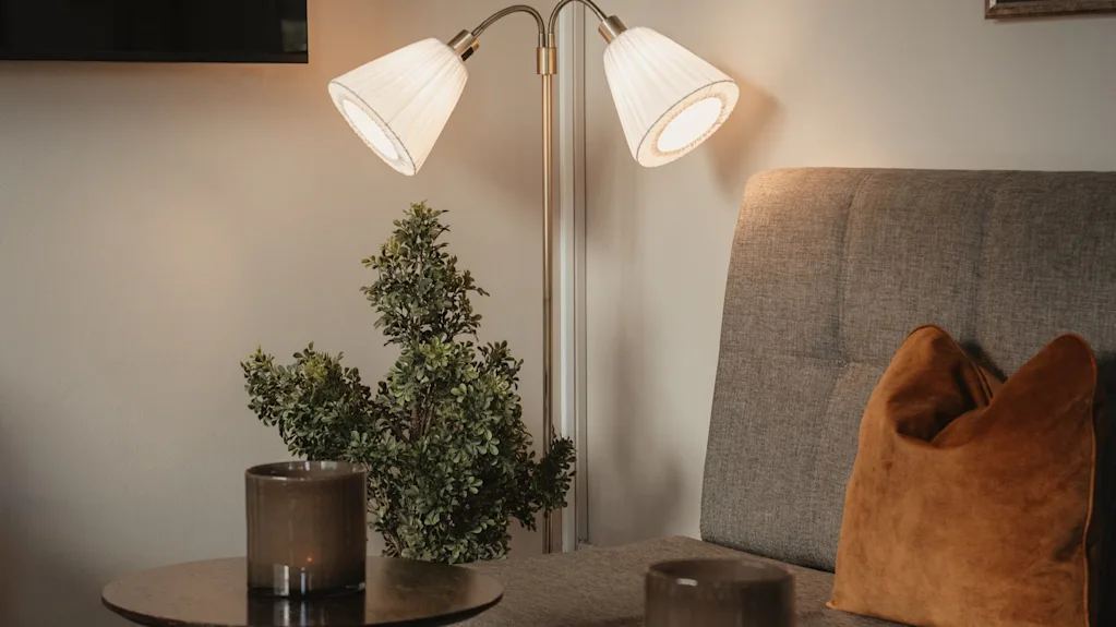 En varm och inbjudande hotellounge med en bekväm soffa, mjuk belysning från en golvlampa och dekorativa inslag.