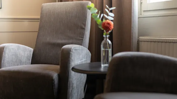 En mysig sittgrupp med två bekväma fåtöljer, ett litet bord med en vas med blommor och varm belysning.