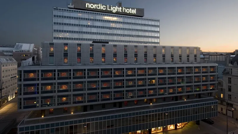 A building with "nordic Light hotel" sign displays lit windows; it's dusk, creating a serene urban setting with a few parked cars on the street below.