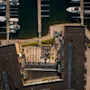 Luftfoto af en livlig marina med fortøjede både, en bygning med en livlig tagterrasse med mennesker og en forfriskende pool.