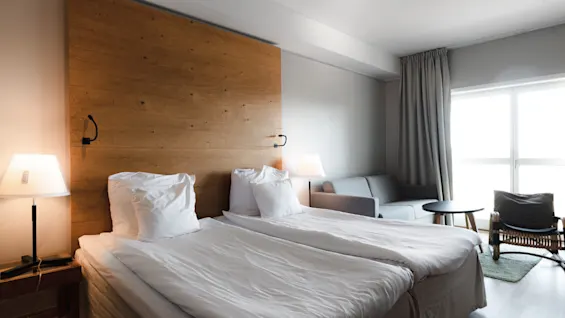 Et lyst og indbydende hotelværelse med to komfortable senge, et hyggeligt siddeområde og naturligt lys.