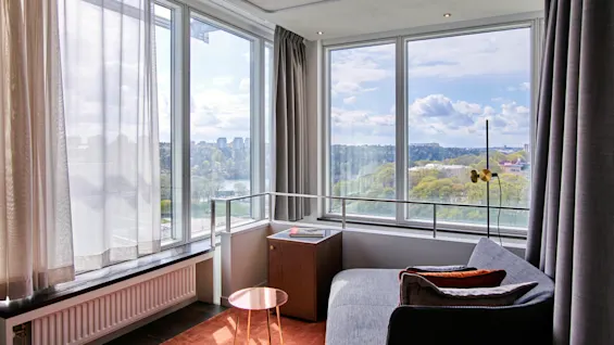 Et lyst hotellrom på Clarion Hotel Stockholm med en komfortabel sofa og et stort vindu som tilbyr en naturskjønn byutsikt.