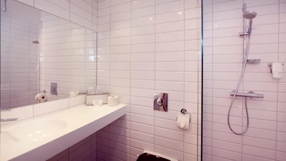 Et rent, hvitfliset baderom med innebygd badekar, dusj og diverse toalettartikler på kanten av vasken.