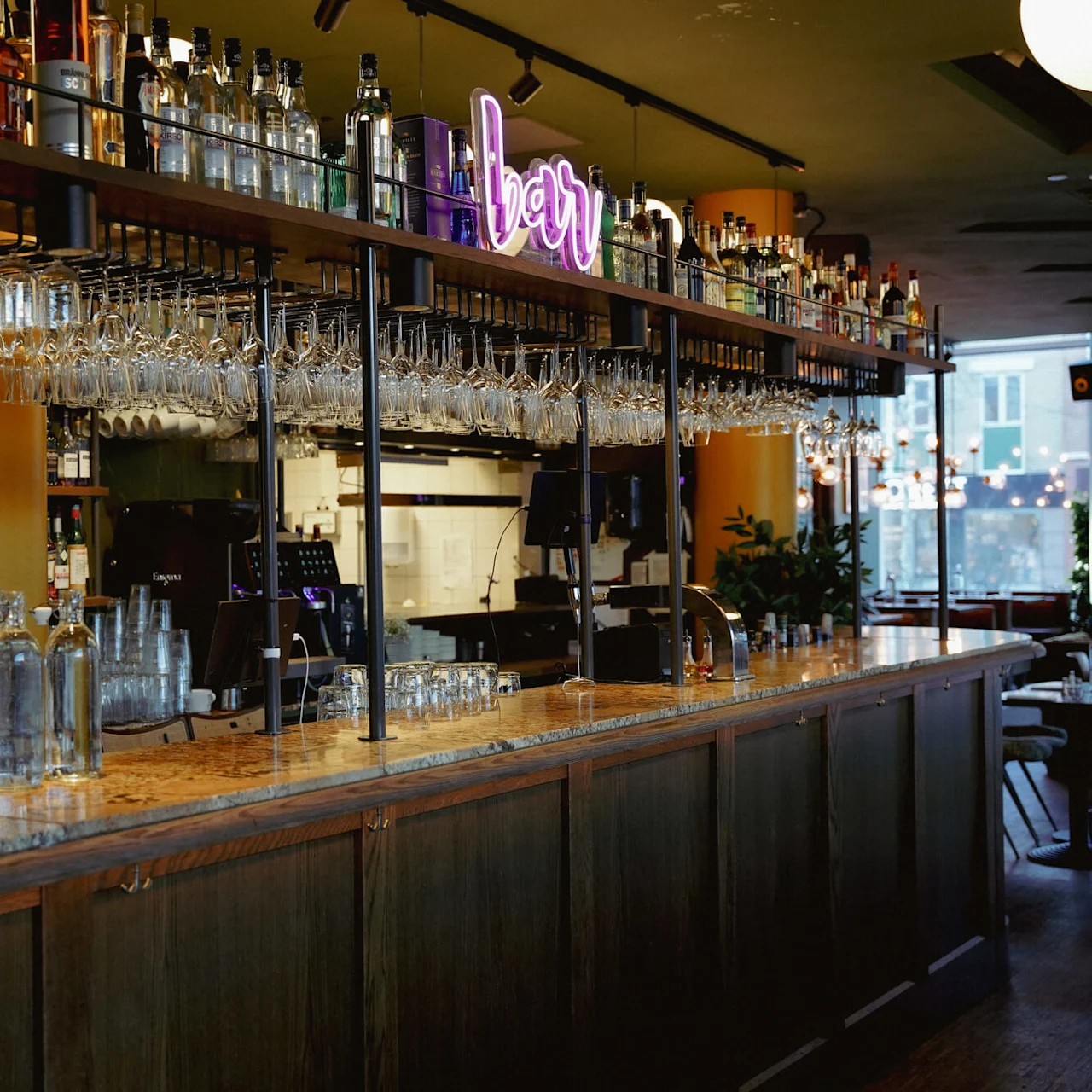 Et velassorteret barområde med hængende glas og et neonskilt "bar" i baggrunden, som afbilleder et stille øjeblik i en bistro-indstilling.