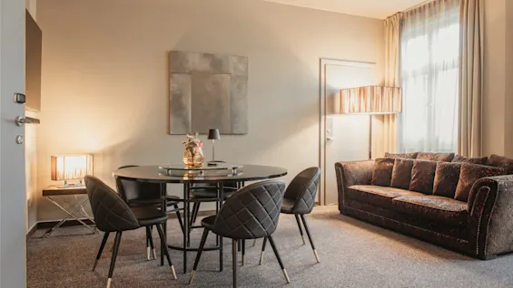 A cozy hotel room with a dining table and chairs, a comfortable sofa, and warm lighting, creating an inviting atmosphere.