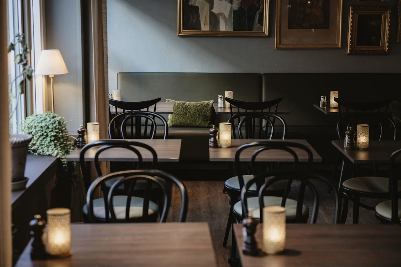 Mysig restauranginredning med mörka träbord, svarta stolar, en grön bänk och varmt levande ljus.