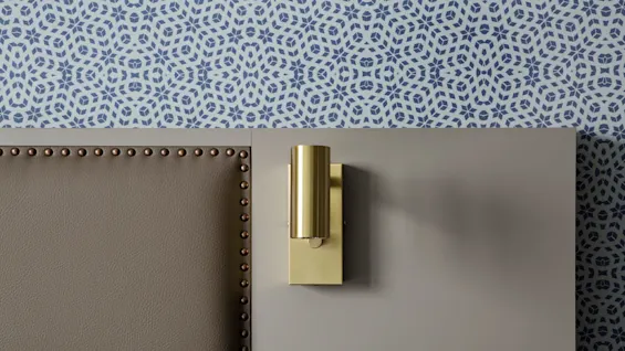 A brass wall lamp mounted on a grey wall, flanked by leather with brass tacks and patterned wallpaper.