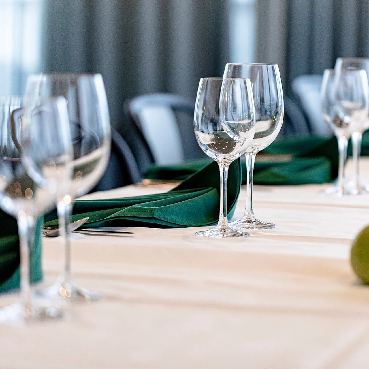 Glassware stands elegantly on a decorated dining table, adorned with dark green napkins and green votive candles, set in a softly lit room.