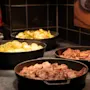 En deilig buffet med varme retter i svarte serveringsskåler, inkludert krydret poteter, blandede grønnsaker og smakfullt tilberedt kjøtt.
