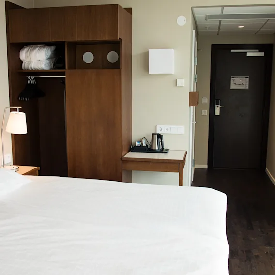 Ett rent och funktionellt hotellrum med en säng, garderob och ett litet bord med en vattenkokare.