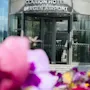 En roterende glassdør merket "Clarion Hotel Bergen Airport" med levende uskarpe blomster i forgrunnen, satt mot en moderne bygning.