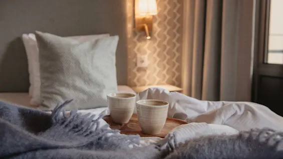 To hyggelige kopper på en bakke i en behagelig seng med et blødt tæppe, perfekt til en afslappende morgen på Home Hotel Wellington.