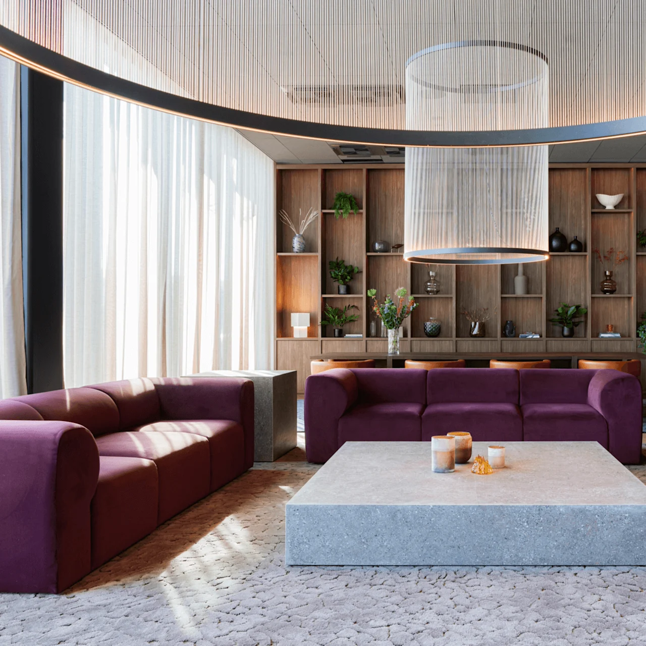 Purple sofas encircle a large stone coffee table, candles atop, in a modern living room with wooden shelving, green plants, and elegant lighting under a ceiling fixture.