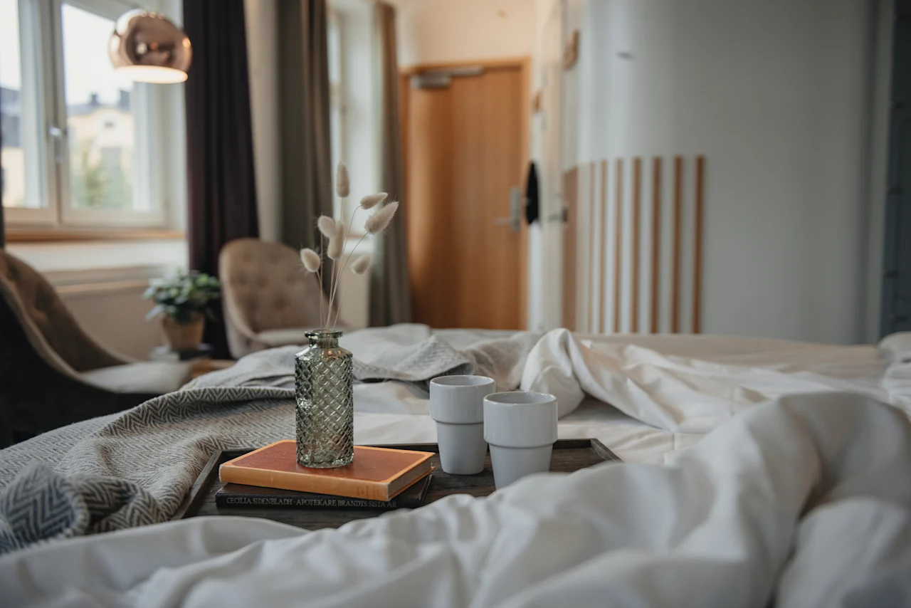 A cozy hotel room at Home Hotel Uppsala with a bed, a tray with books, dried flowers, and two cups, ready for a relaxing moment.