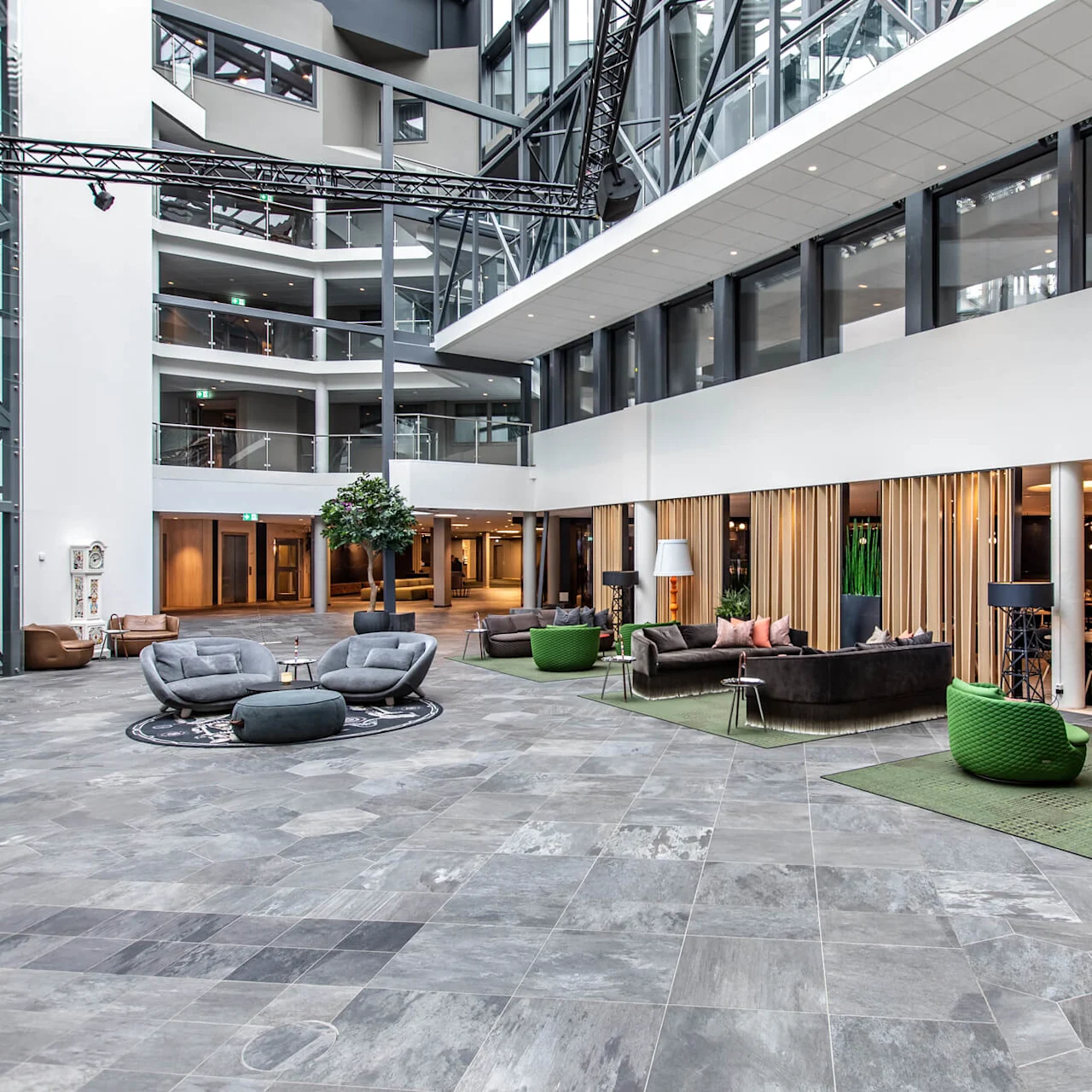 Modern lobby with gray and green seating and tables, surrounded by open spaces and large windows, creating a contemporary and inviting atmosphere in a spacious building.