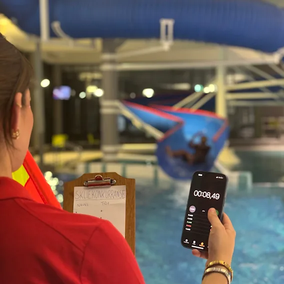 En badevakt som tar tiden på en skliekonkurranse med smarttelefon i et innendørs badeland.