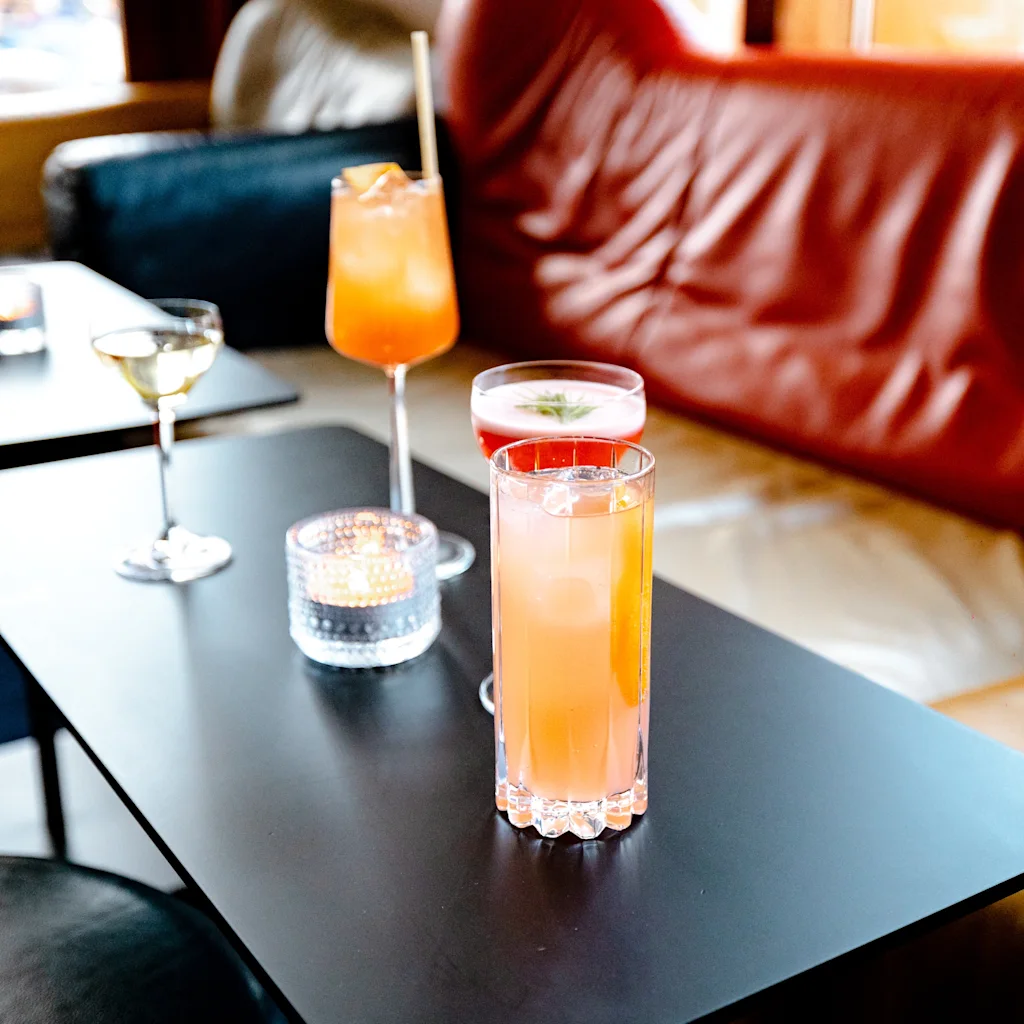 Et koselig salongmiljø med ulike fargerike drinker på et bord, som antyder en avslappet sosial atmosfære.
