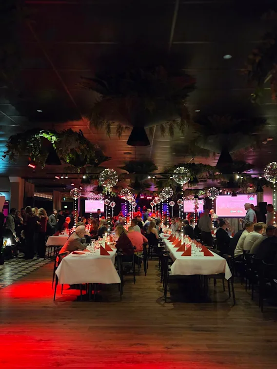 En stor festsal fylld med gäster som sitter vid långbord under en julfest.