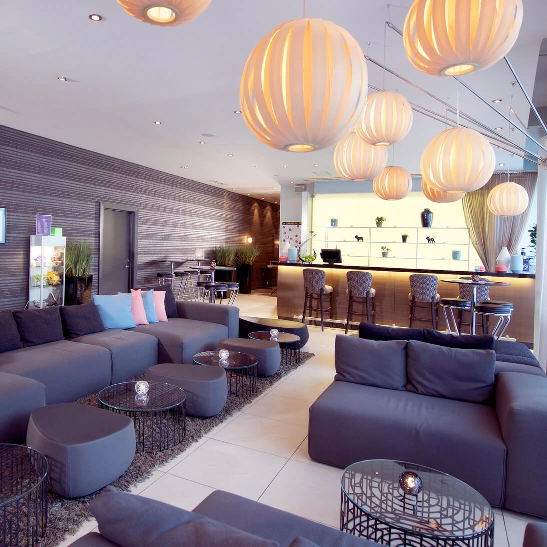 A modern hotel lobby with comfortable seating, hanging spherical lamps, and a reception desk, providing a welcoming ambiance for guests.