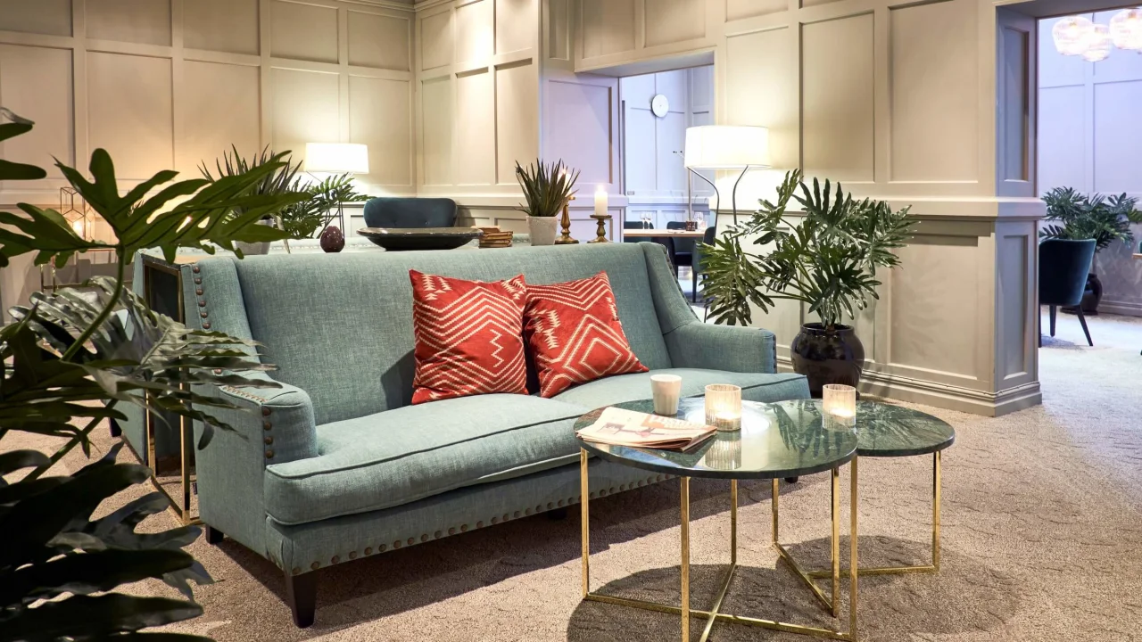 A teal sofa with red pillows and a gold-framed coffee table in a cozy, well-lit living room.