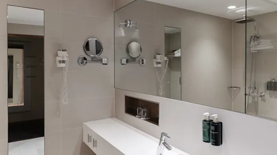 Ett rent och modernt hotellbadrum med en rymlig kommod, stor spegel och ett välutrustat duschutrymme.