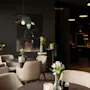 En stilig, dempet opplyst restaurant eller lounge med komfortable sitteplasser, planter og et stort kunstverk på en mørk vegg.