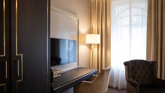 Et veloplyst hotelværelse med en funktionel arbejdsplads med skrivebord og stol, et fjernsyn og en afslappende lænestol ved vinduet.