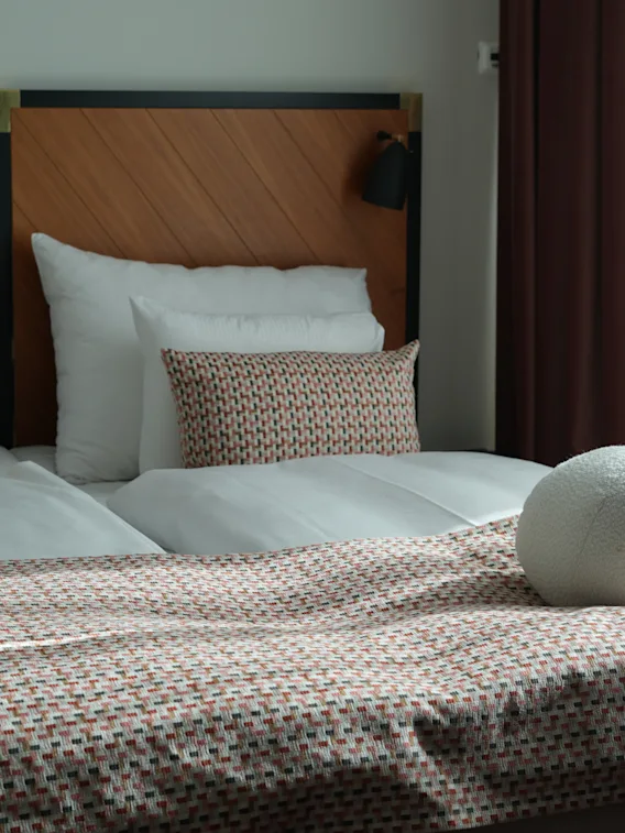 En hyggelig hotelseng med hvide puder, mønstrede pynteputer og en rund dekorativ pude.