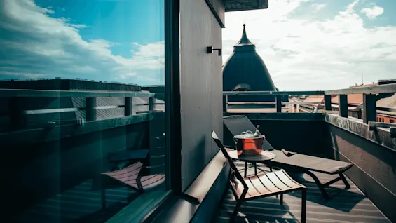 Stol og solseng på en balkong med et lite bord som har en champagneflaske i en isbøtte. Utsikt over tak og en skyet himmel.