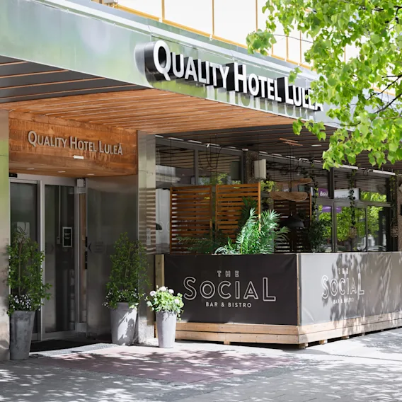 Entré till ett Quality Hotel med en inbjudande uteservering för The Social Bar & Bistro, omgiven av grönska.