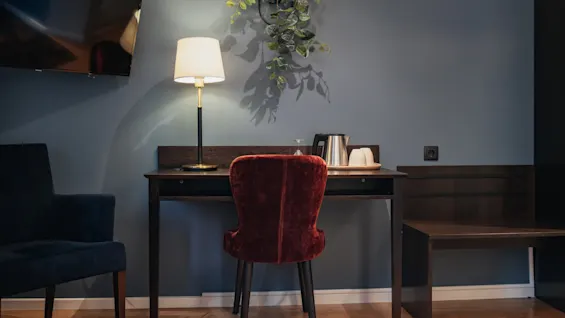 A well-lit desk area in a modern hotel room, featuring a lamp, kettle, and a comfortable red chair. Home Hotel Kung Oscar.