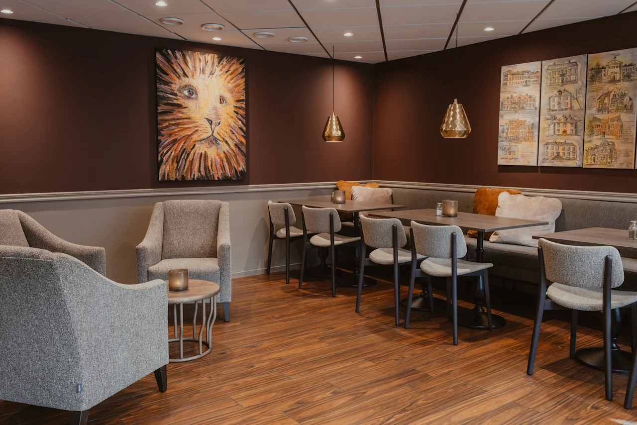 Ett mysigt loungeområde med bekväma sittplatser, bord och varm belysning, med en stor lejonmålning på väggen.