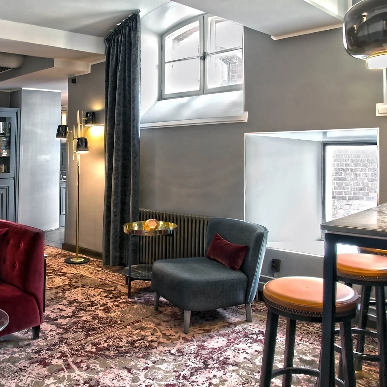 An elegant lounge with a plush red sofa, curated bookshelves, framed portraits, and ambient lighting creates a cozy atmosphere.