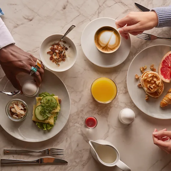 Två personer njuter av en härlig frukostbuffé med kaffe, juice, bakverk och salta rätter på ett marmorbord.