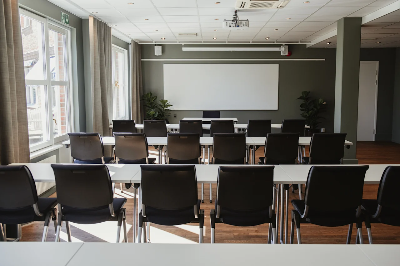 Ett väl upplyst konferensrum med bord och stolar vända mot en whiteboard och projektor, redo för möte eller presentation.
