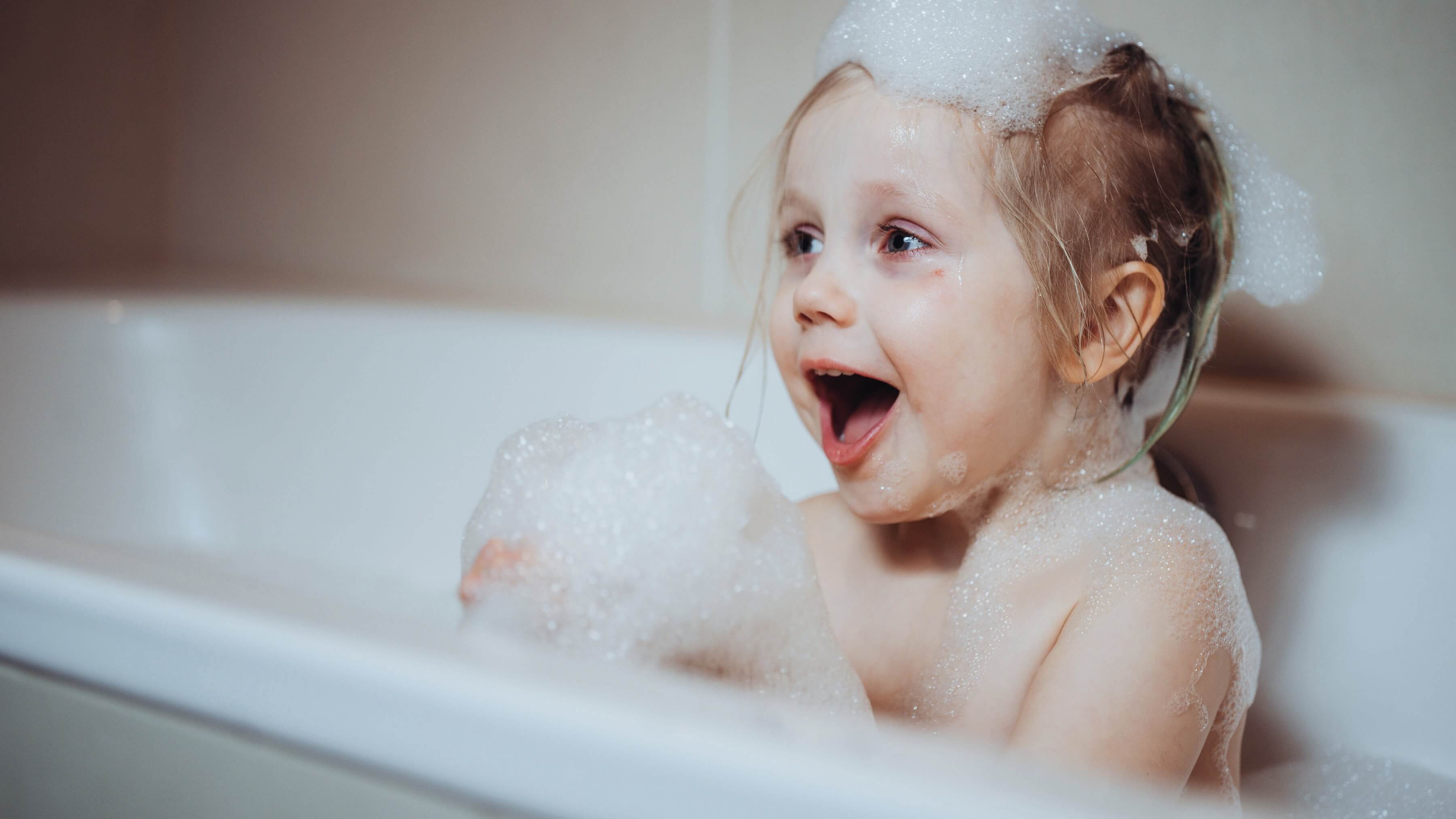 Et lykkelig barn bader i et badekar omgitt av bobler, uttrykker glede.