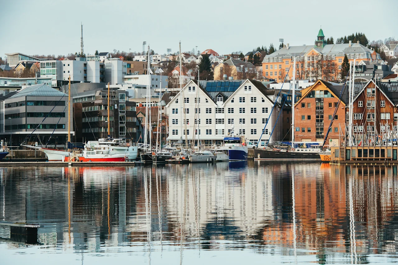 A scenic waterfront view of a city with buildings and boats reflected in the calm water.
