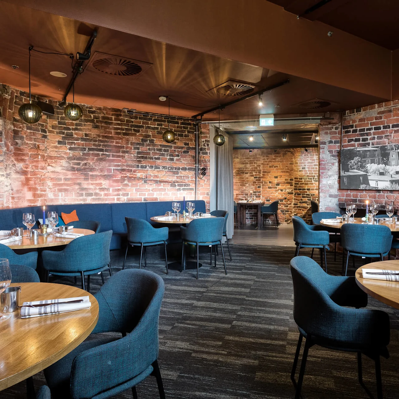 A cozy restaurant interior with set tables, blue chairs, and exposed brick walls, creating an inviting dining atmosphere.