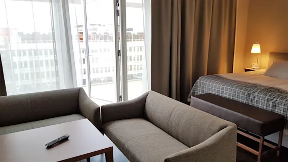 Mukava hotellihuone, jossa oleskelutila sohvineen ja sohvapöytineen, sekä makuutila sänkyineen ja yöpöytälamppuineen.