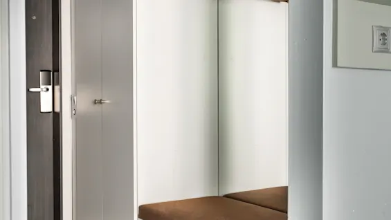 En minimalistisk hall med en garderob med spegel och en mysig brun bänk. Trähängare är redo för rockar, vilket ger en varm känsla till den eleganta designen.
