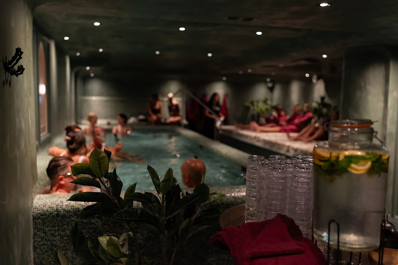 Ihmiset nauttivat rentouttavasta ajasta hämärästi valaistussa sisäuima-allas- ja spa-alueella, jossa on tarjolla virkistävää sitruuna- ja minttuvettä.