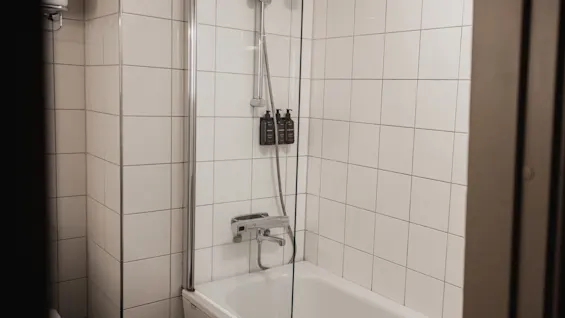 A modern bathroom featuring a white tiled shower and bathtub area with wall-mounted dispensers for toiletries.