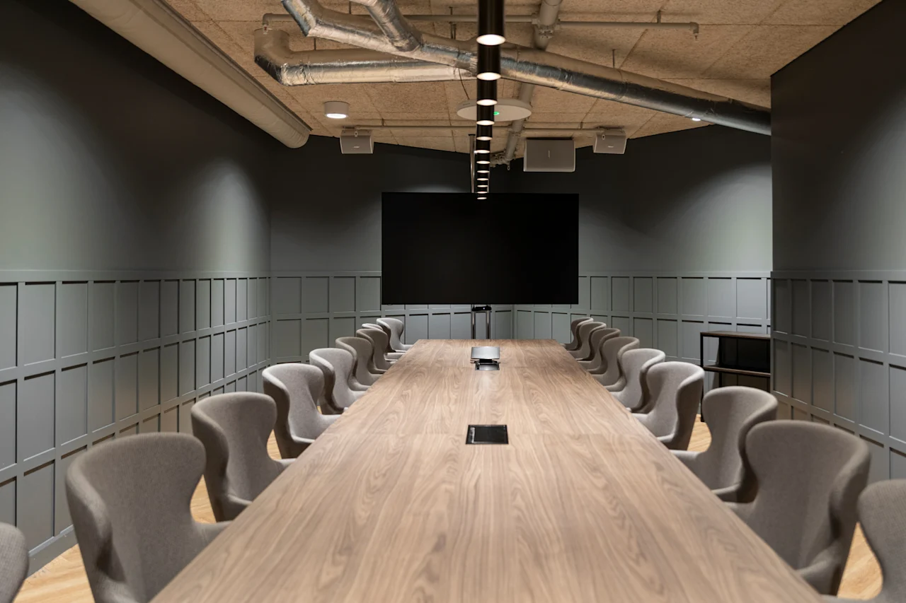 A sleek, modern conference room featuring a long wooden table, comfortable chairs, and a large screen for presentations.