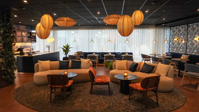 Sisustusalue modernien sohvien ja tuolien kanssa on järjestetty pienten pöytien ympärille. Tunnelmalliset riippuvalaisimet luovat kodikkaan ilmapiirin tyylikkäästi sisustettuun loungeen.