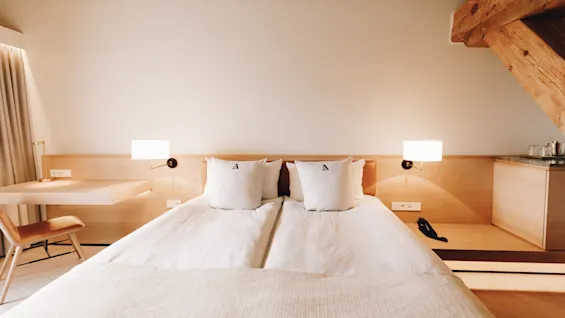 Ett ljust, modernt hotellrum med en stor säng, ett skrivbord och varm belysning, med en träbalk.