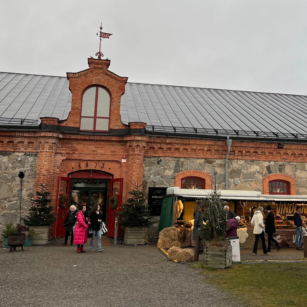 Folk der besøger udendørs markedsboder ved siden af en historisk rød murstensbygning