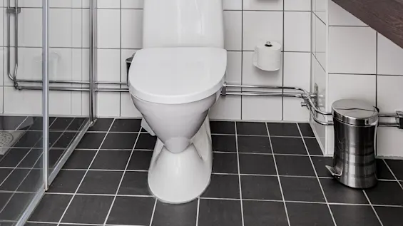 A modern bathroom with white toilet, towel rack, and glass shower enclosure. Black and white tiled floor with clean lines.