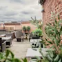 A rooftop terrace with outdoor seating, lush green plants, and a brick wall under a cloudy sky.